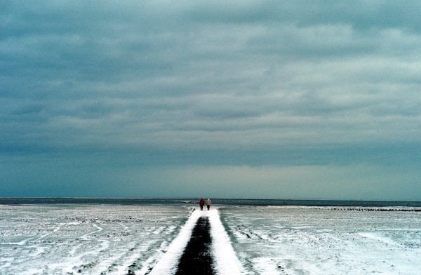 Pedestrians stroll at icy mudflat of Westerhever, Germany.