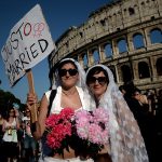 A couple dressed as brides holds a placard reading "Just married". Photo: Filippo Monteforte/AFP