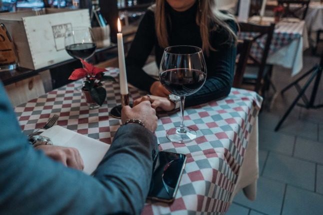 A couple hold hands as they share dinner and a glass of wine in Austria. Photo by René Ranisch on Unsplash