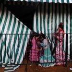 Young girls wear traditional Sevillana dresses in a <i>caseta</i> or small house. The fairgrounds are lined with these tents, which usually belong to prominent families or organizations in Seville.Photo: Cristina Quicler / AFP.