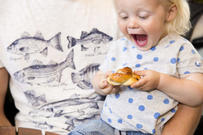 A smiling child eats a Swedish cinnamon bun