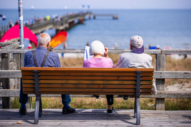 Three older people sit on a bench in Prerow, northern Germany in summer 2021.