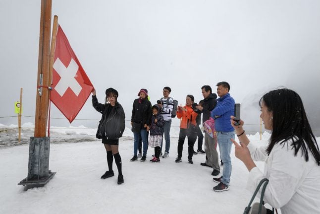 An enthusiastic person stands in front of a Swiss flag. 