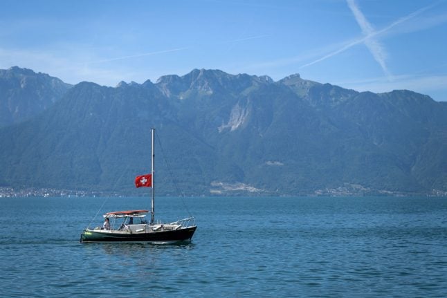 A boat sails on Lake Geneva under a Swiss flag.