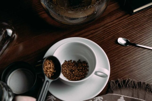 A person spoons instant coffee granules into a cup. Photo by Amr Taha on Unsplash