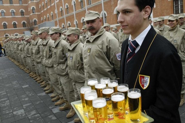 A waiter holds beers as he stands next to Austrian soldiers at a ceremony in Vienna.