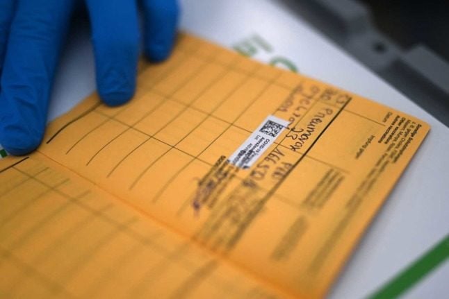 A close up of a vaccination card as a doctor enters details about a Covid jab. How do you prove you have had the virus in Austria? Photo: INA FASSBENDER / AFP