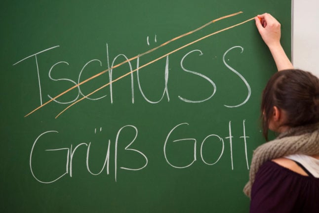 A teacher scores out "Tschüss" and writes regional greeting "Grüß Gott" on a board.