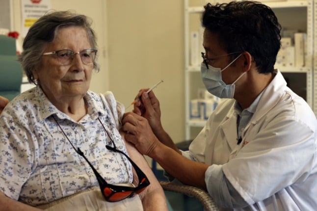 An older woman receives an injection of Covid-19 vaccine in her arm from a medical professional