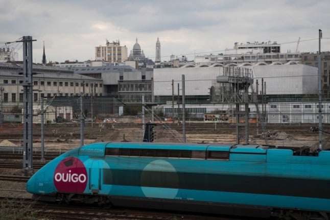 A blue high-speed Ouigo low-cost TGV train arriving at  de l'Est railway station in Paris, with the the Sacre-Coeur Basilica in the background