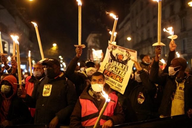 Protesters hold candles and placards during a demonstration for the regularisation of migrants on International Migrants Day in Paris.
