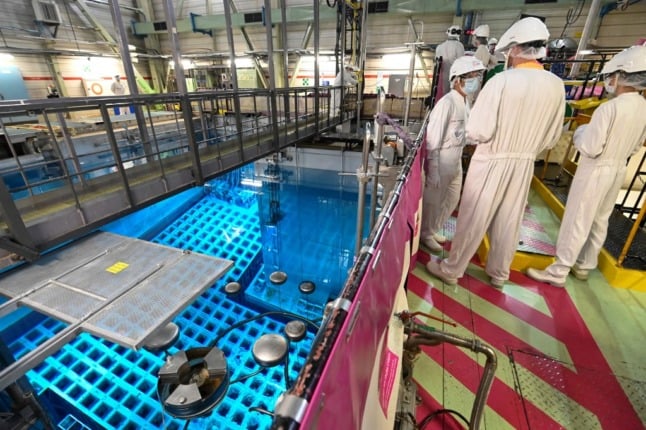 Workers in white overalls remove a nuclear fuel bar from a pool of coolant water at the shut-down nuclear power station at Fessenheim
