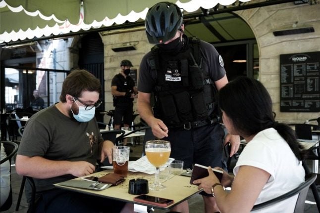 A policeman checks health passes at a bar in Bordeaux. The pass could eventually be lifted for outdoor dining.