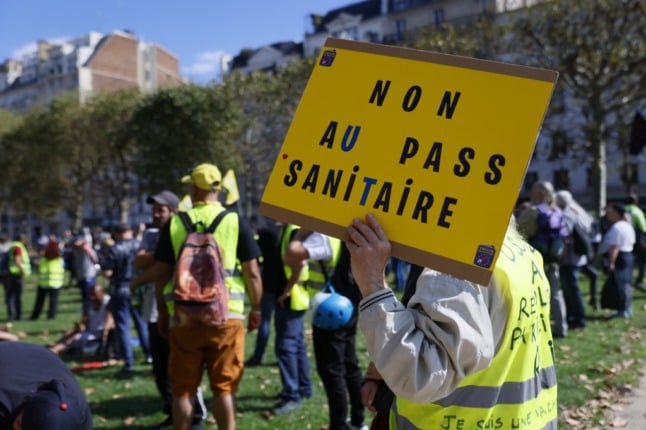 A protester wearing a hi-visibility vest holds up a sign reading 'Non au pass sanitaire' during a protest in France