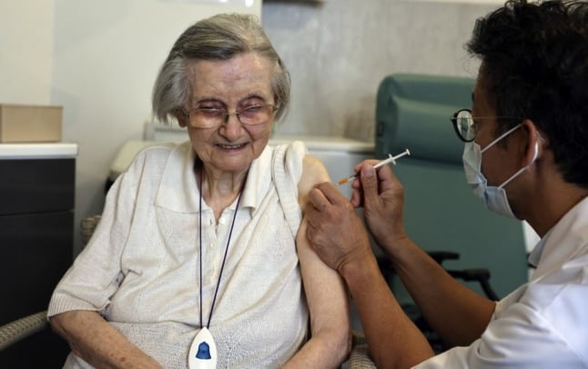 An older woman in France receives a Covid-19 injection in her left arm from a doctor wearing a facemask