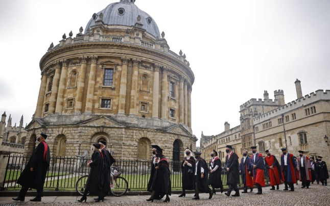 University members in black or red gowns and wearing mortar boards walking outside at Britain's Oxford University