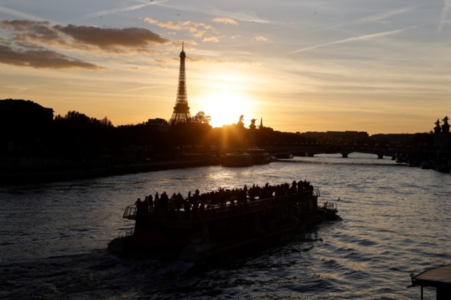 A tourist boat on the Seine river in front of the Eiffel Tower at sunset in Paris