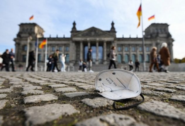 A protective face mask is seen on the ground as passers-by walk in front of the Reichstag building housing the lower house of parliament Bundestag in Berlin, Germany,.