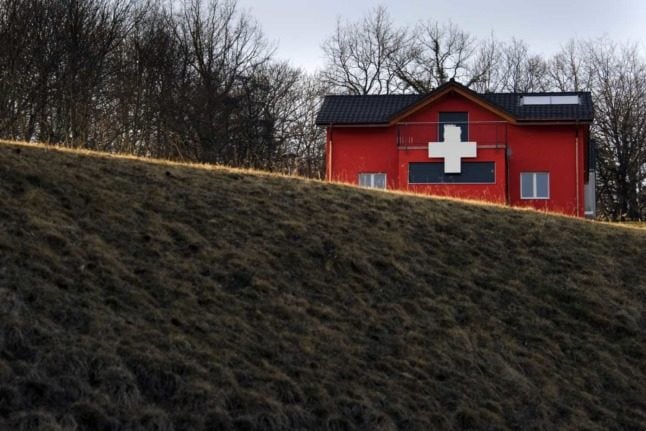 A house painted in Swiss flag colours sits in the middle of a meadow in Switzerland.