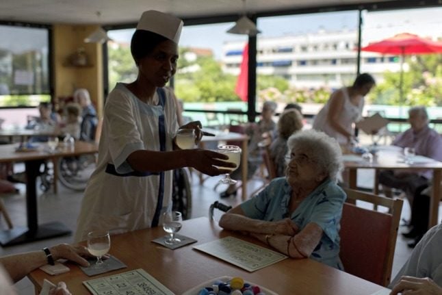 A nurse serving drinks to elderly residents at a care home in France while they play bingo