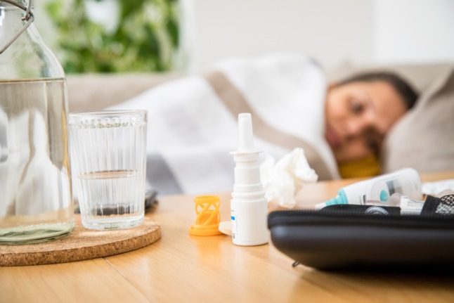 A woman lies on the sofa with medicine for a cold