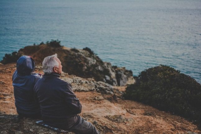 Two older people sitting on the floor looking out over a body of water