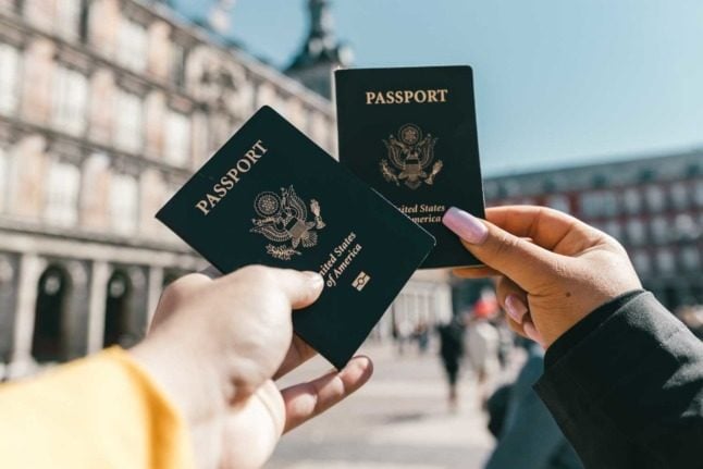 Two people hold up their American passports in a European town square
