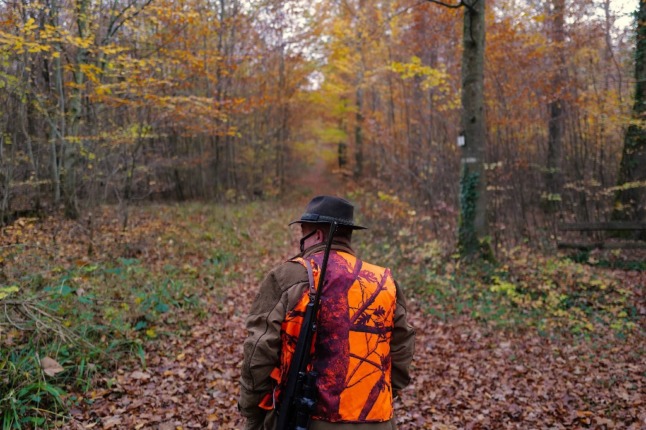 A hunter in a hi-vis vest, with a gun over his shoulder, walks along a woodland path in Hirsingue, eastern France