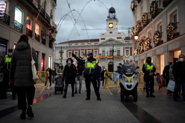 Spanish police officers stand guard as people shop for Christmas in the centre of Madrid on December 7, 2020. OSCAR DEL POZO / AFP