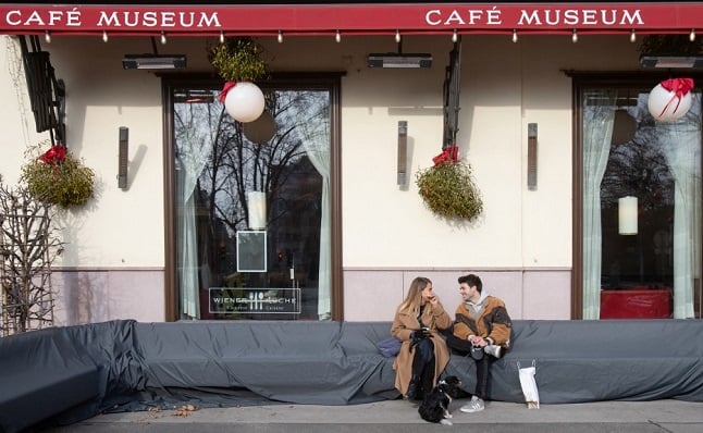 A couple with a dog sit in front of the Cafe Museum in Vienna on February 1, 2021. 