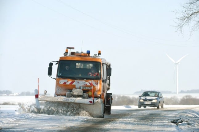 An orange snowplough, followed by a private car clears overnight snowfall from a country road in central France