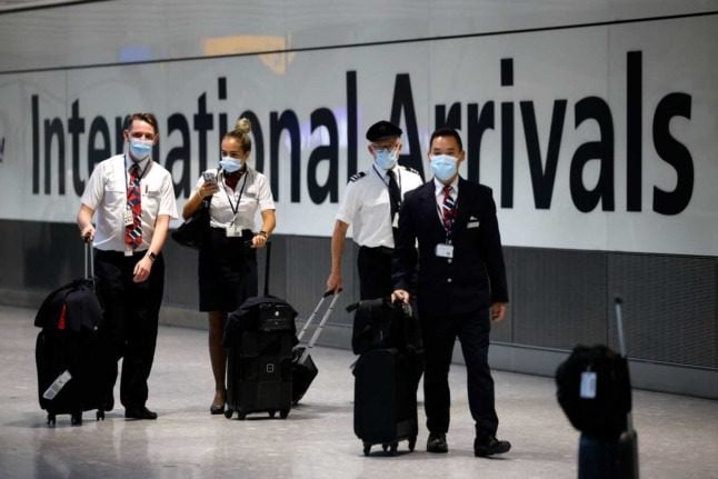 Airline staff in masks walk past an international arrivals sign at Heathrow Airport