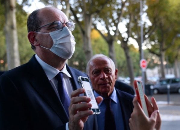 French Prime Minister Jean Castex, wearing a facemask, holds up his mobile phone to show an official his digital Covid-19 health pass before he can enter a political event