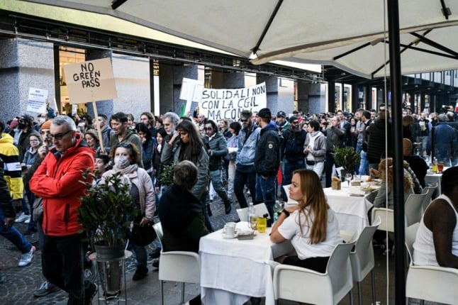 Anti-green pass protestors walk past restaurants in Milan.