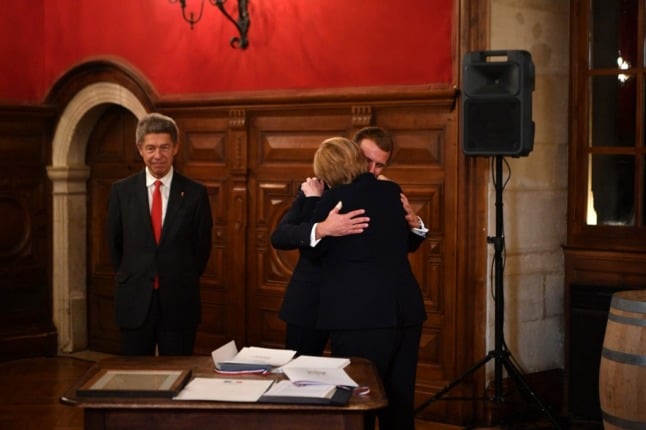 Macron and Merkel embrace, watched by Merkel's husband Joachim Sauer  