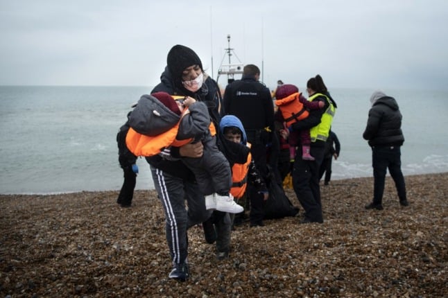 A migrant carries her children after being helped ashore from a RNLI (Royal National Lifeboat Institution) lifeboat at a beach in Dungeness, on the south-east coast of England, on November 24, 2021, after being rescued while crossing the English Channel. - The past three years have seen a significant rise in attempted Channel crossings by migrants, despite warnings of the dangers in the busy shipping lane between northern France and southern England, which is subject to strong currents and low temperatures. (Photo by Ben STANSALL / AFP)