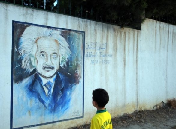 A boy looks at a wall showing a graffiti painting of Albert Einstein in Tunis,