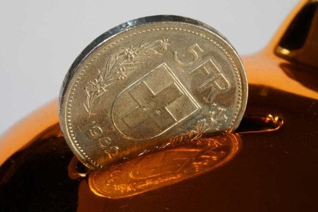 A five franc coin is put into a shiny piggy bank 
