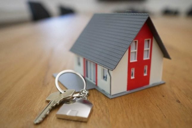 A small plastic house sits next to a key on a wooden surface