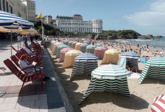 A woman reads a book on a deckchair as people walk next to parasols on the 