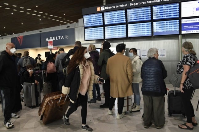 Delta Airline passengers stand near a departures board at Charles de Gaulle airport in Paris