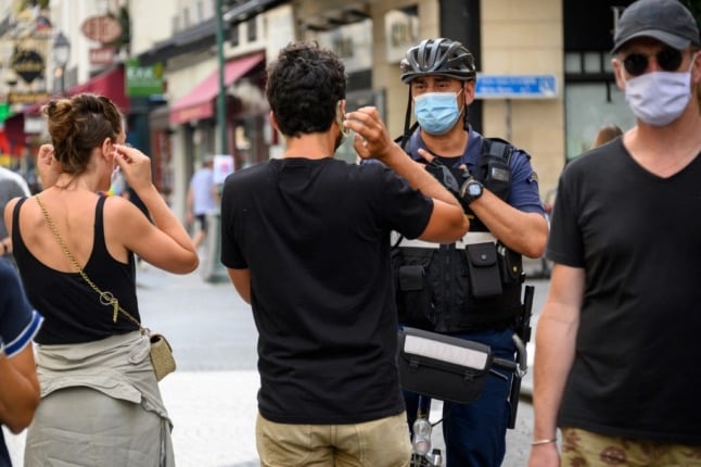 A Paris municipal police officer wearing a face mask asks people to put on their masks