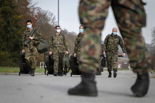 Swiss military members walk across a road carrying guns