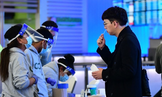 A traveller, watched by a masked member of testing staff, swabs his nose at a rapid Covid-19 test site at a US airport