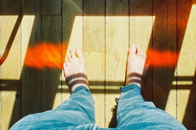 A person stands on wooden floorboards with bare feet