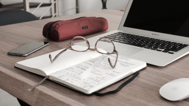 Pictured is a laptop and accountancy notes. 