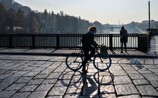 A woman rides a bike in downtown Turin, Piedmont: one of the Italian regions becoming an 'orange' zone on Monday.