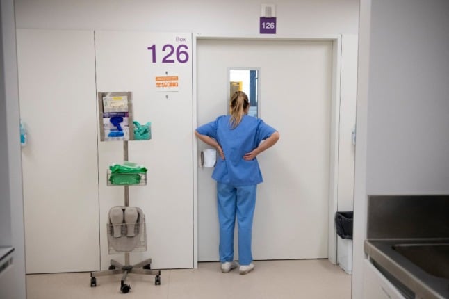 A healthcare worker watches a Covid-19 patient through the door, at the semi-critical respiratory unit of the Bellvitge University Hospital in Barcelona on January 19, 2022. - Milder for most but still highly contagious, Omicron has filled intensive care beds again at a hospital near Barcelona where shattered staff are still fighting a virus that refuses to retreat. (Photo by Josep LAGO / AFP)