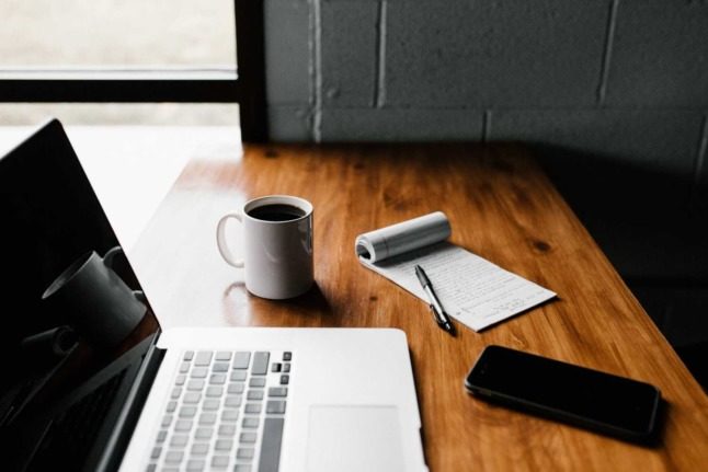 A computer next to a pad and a cup of coffee on a wooden table