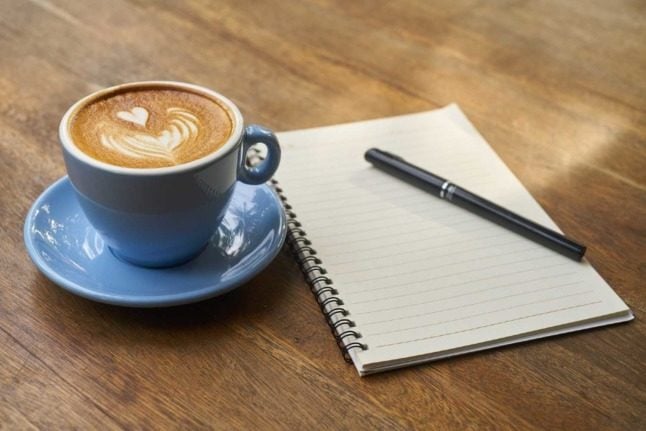 A cup of coffee next to a notebook sitting on a wooden table